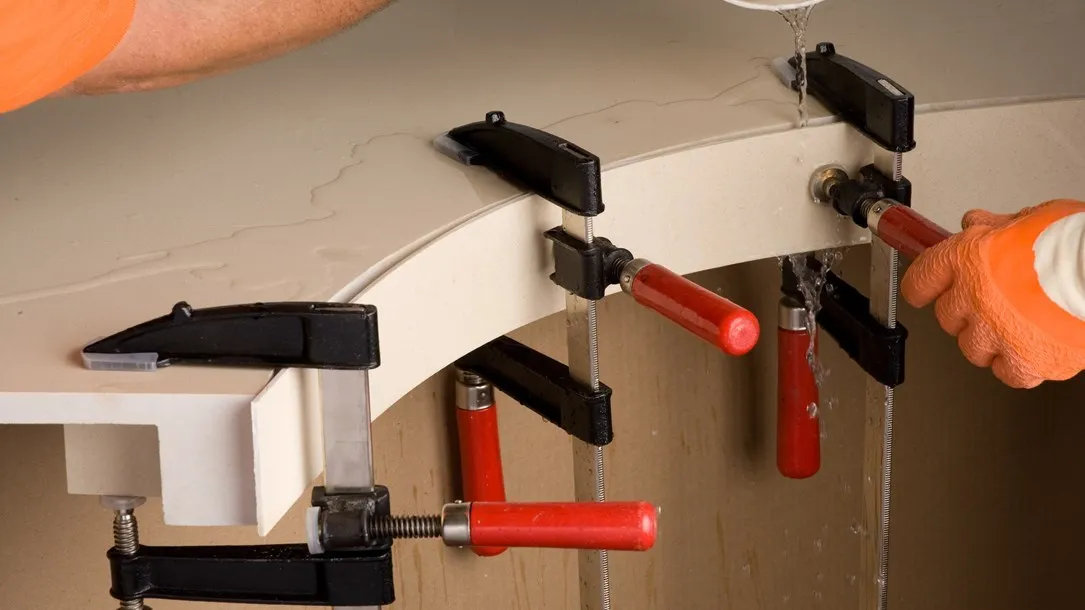 Fabricator shaping a curved Caesarstone quartz surface with clamps and water during the thermoforming process.