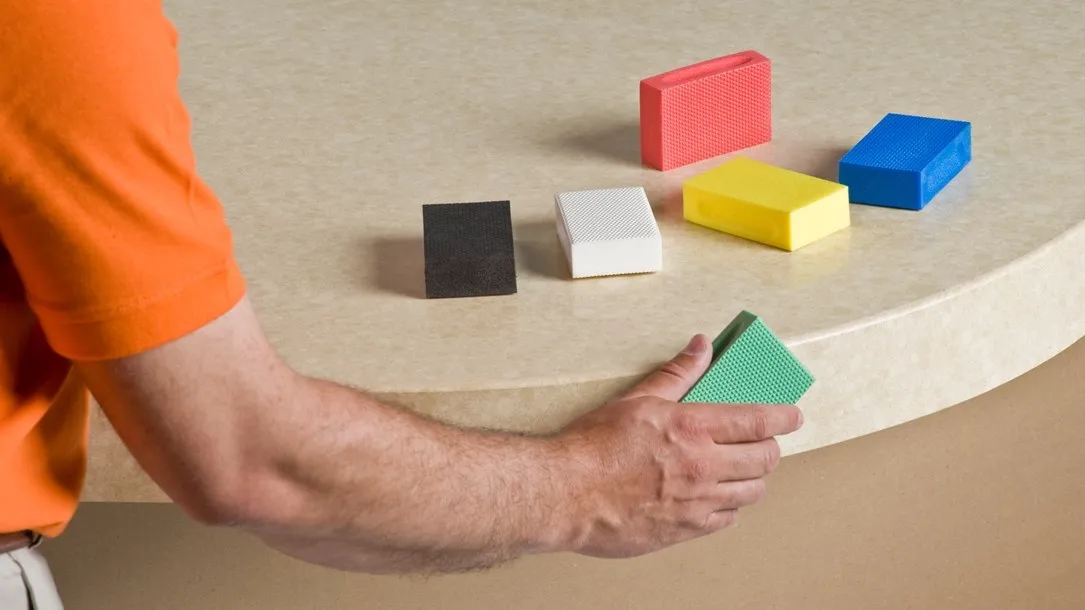 Worker hand-finishing a curved Caesarstone thermoformed quartz surface using colored sanding blocks.