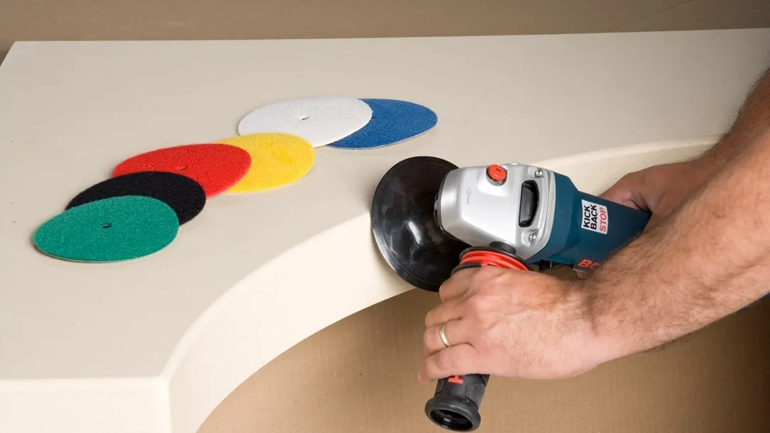 Worker polishing a curved Caesarstone thermoformed quartz surface with a power tool and sanding discs.