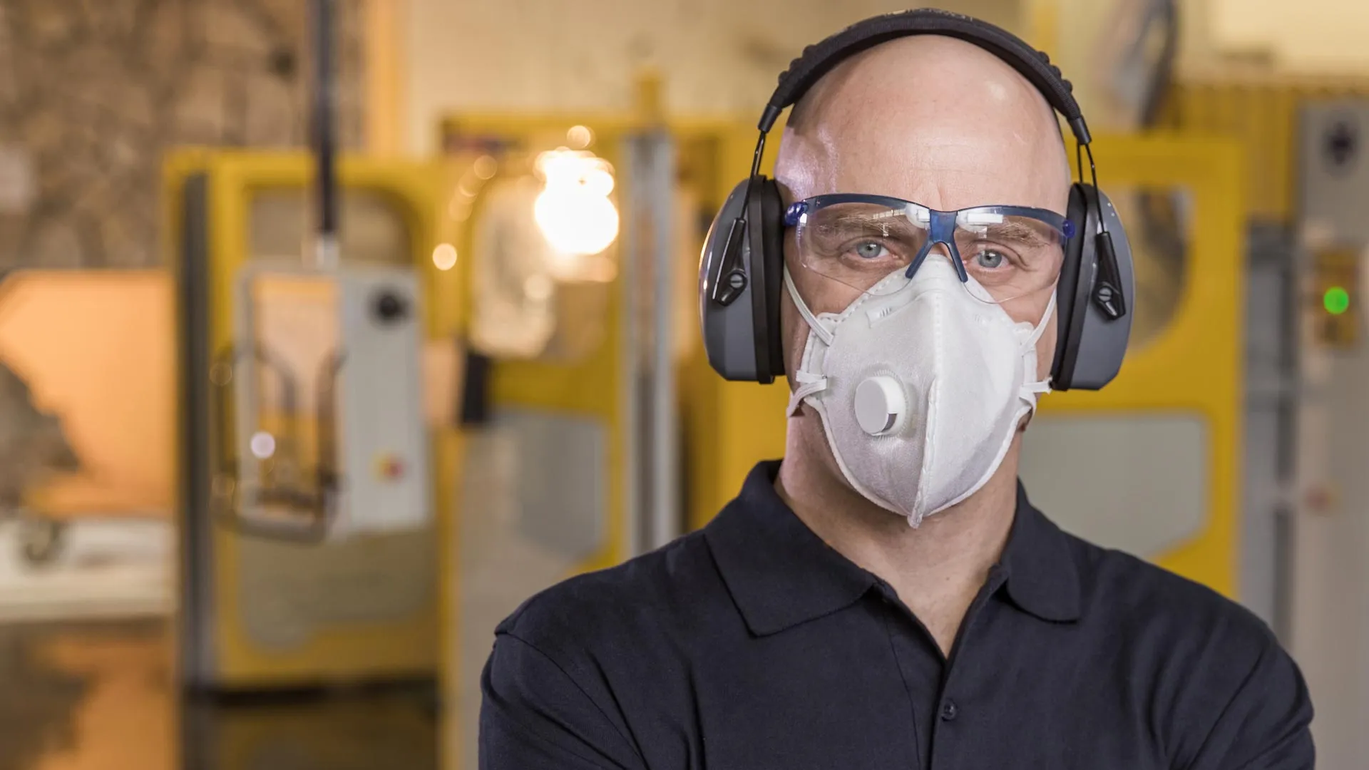 Fabricator wearing protective gear including a respirator mask, safety glasses, and earmuffs, standing confidently in a Caesarstone workshop.