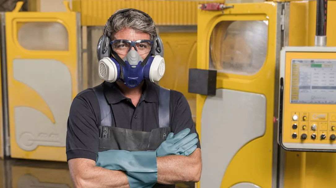 Fabricator wearing protective gear including a respirator mask, safety glasses, and earmuffs, standing confidently in a Caesarstone workshop.